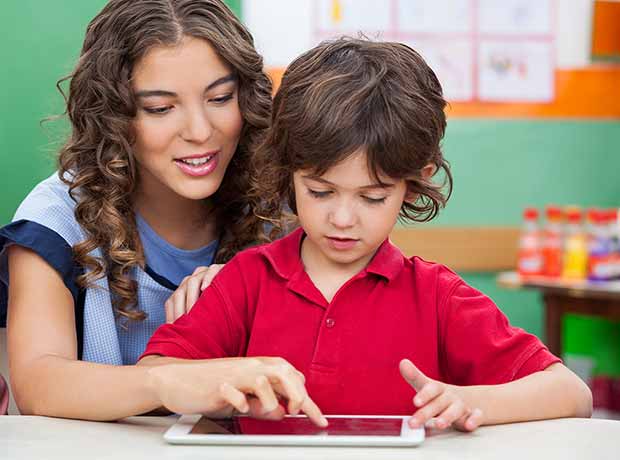 Photo of a teacher showing a young boy something on an iPad.