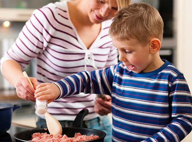 photo of a young boy cooking, helped by a teacher.